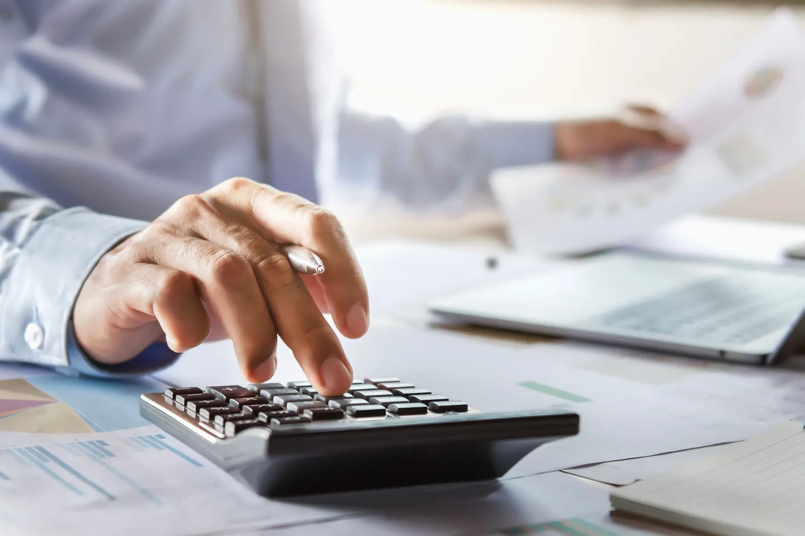 Des mains calculent un montant sur un bulletin de salaire et un avis d'imposition